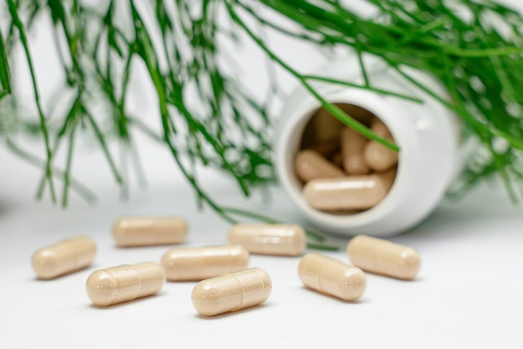 Beige herbal supplement capsules spilled from bottle on clean white counter with botanical background