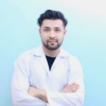 Dr. Hasnain Siraj Memon wearing a lab coat with arms crossed and a confident smile