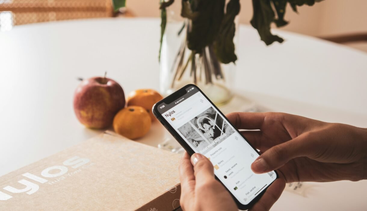 Person using smartphone to track health data with fruits and a wellness box on the table.